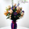 Bouquet of pale roses and purple flowers in a purple vase with ribbon