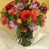 Mixed bouquet of roses, carnations, and purple daisies in a glass vase