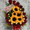 Arrangement of yellow sunflowers and red roses with gold-wrapped chocolates in a wooden box with a red bow and card.