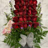 Tall arrangement of tiered red roses with small purple asters in a metal container with a silver bow