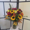 Mixed bouquet of sunflowers, roses, and lilies in a clear glass vase