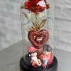 Red decorative rose under a clear dome with two small figurines at the base