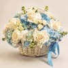 White roses and blue hydrangeas in a wicker basket with a blue ribbon
