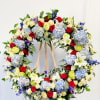 Large floral wreath of red, white, blue, and pale yellow flowers on a wooden stand