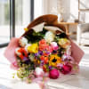 Mixed bouquet of roses, sunflowers, and daisies wrapped in pink paper