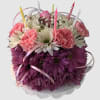 Pink and purple flower arrangement with striped candles in a white container