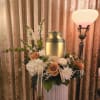 Floral arrangement with white and peach roses beside a gold urn and lamp