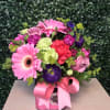 Pink and purple mixed flower arrangement in a pink box with a ribbon