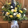 Large floral arrangement with yellow roses, white blooms, and blue flowers in a white vase