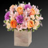 Bouquet of peach roses, purple carnations, and pink flowers in a wooden cube vase