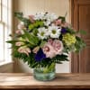 Mixed bouquet of white daisies, pink blooms, and purple accents in a glass vase