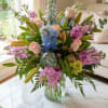 Mixed bouquet of pink roses, blue hydrangeas, and lilies in a glass vase
