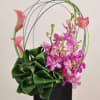 Pink calla lilies and orchids in a black vase with arched stems