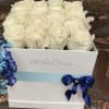 White roses arranged in a white gift box with blue ribbon accents.