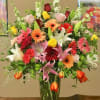 Mixed bouquet of roses, lilies, and gerbera daisies in a tall glass vase