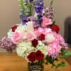 Mixed bouquet of roses, hydrangeas, and purple flowers in a glass vase