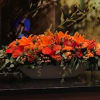 Long orange floral arrangement with roses and lilies in a low container