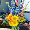Colorful bouquet with sunflowers, roses, and blue delphinium in a glass vase
