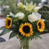 Bouquet of sunflowers, white roses, and pale lilies in a glass vase
