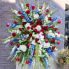 Tall standing spray with red roses, white hydrangeas and orchids, and blue delphinium on an easel