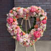 Large heart-shaped floral wreath in pink, peach, and white blooms on an easel