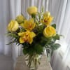 Yellow roses and orchids arranged in a clear glass vase