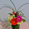 Bright gerbera daisies and hydrangeas in a green vase with tall tropical leaves