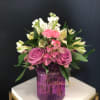 Pink and white flower arrangement in a purple glass vase