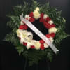 Circular funeral wreath with red and white flowers and a white ribbon