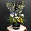 Tall mixed bouquet in a dark glass vase with blue, white, and yellow flowers