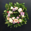 Circular wreath of pastel roses and greenery on a dark stand