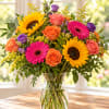 Mixed bouquet of sunflowers, roses, and gerbera daisies in a glass vase