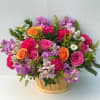 Mixed bouquet of pink, purple, and orange flowers in a wooden basket