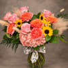 Pink and coral flowers in a glass vase with a bee-patterned ribbon