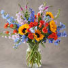 Colorful bouquet of sunflowers, roses, and blue flowers in a clear glass vase