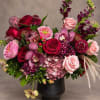 Mixed bouquet of red, pink, and purple flowers in a black vase