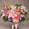 Pink and peach bouquet with lilies, roses, and purple flowers in a glass vase