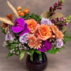 Mixed bouquet of orange, lavender, and purple flowers in a dark glass vase