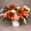 Mixed bouquet of orange, pink, and cream flowers in a white vase