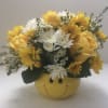 Yellow and white flower arrangement in a smiley-face container