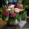 Low floral arrangement with pink and burgundy blooms in a metal bowl