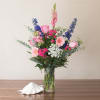 Tall pink, blue, and white mixed flower arrangement in a clear glass vase on a table