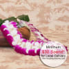 Purple and white orchid lei draped beside a wooden bowl on a patterned surface