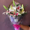 Hand-tied bouquet of pink and white lilies with buds, wrapped in clear paper with a bright pink ribbon bow
