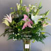 Tall arrangement of pink and white lilies with buds in a clear glass vase with ferns.