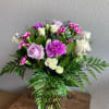 Mixed bouquet of lavender roses, white roses, and purple carnations in a clear glass vase