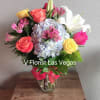 Bright mixed bouquet of roses, lilies, hydrangea and alstroemeria in a clear glass vase on a wooden crate.