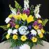 Mixed floral arrangement with yellow lilies, white blooms, and purple flowers in a white vase