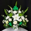 White floral arrangement with lilies, roses, and green shamrock picks in a white vase