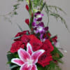 Tall bouquet of red roses, pink lily, and purple orchids in a glass vase